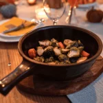 Pentola in ceramica con verdure cotte al forno posizionata su una tavola apparecchiata con atmosfera calda e accogliente, stile editoriale